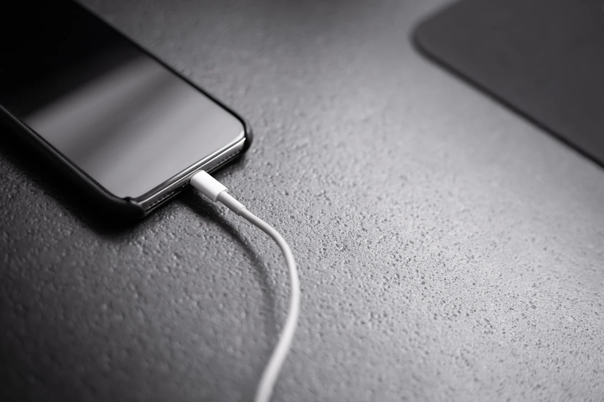 Smartphone lying on a dark surface with a charging cable plugged in